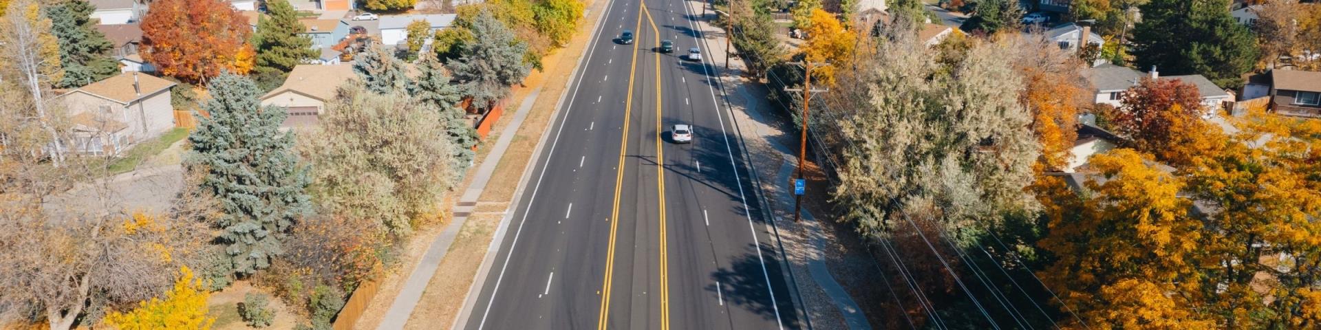 Aerial view of a wide street lined with houses and colorful autumn trees.