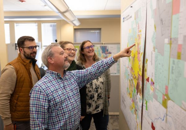 Four people smile and look at a map.